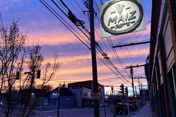 Street scene at sunset with restaurant sign and colorful sky.